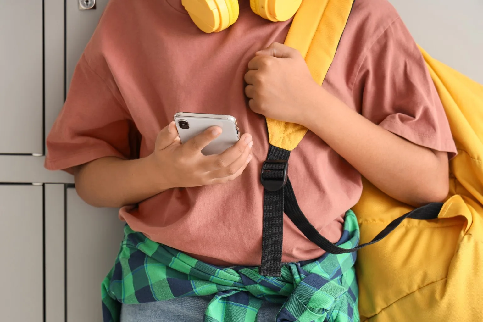 Child in school corridor, on smartphone.
