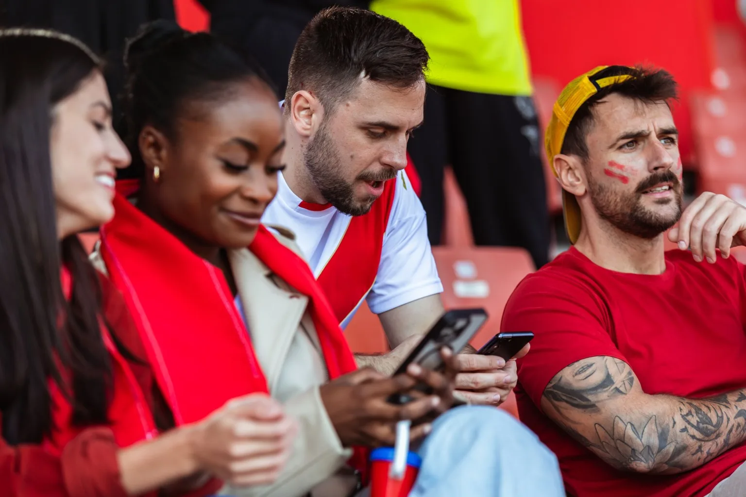 Four friends sat in crowd at sports game, with some on their phones.