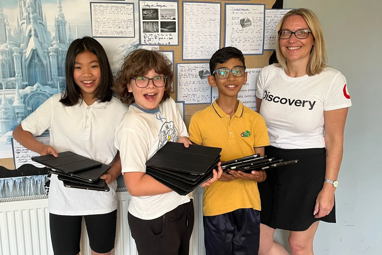 Three children and a VodafoneThree staff member stood in school holding iPads.