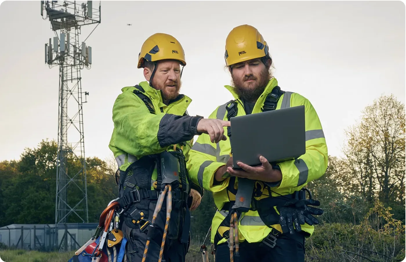 Two network engineers with a laptop in front of mast.