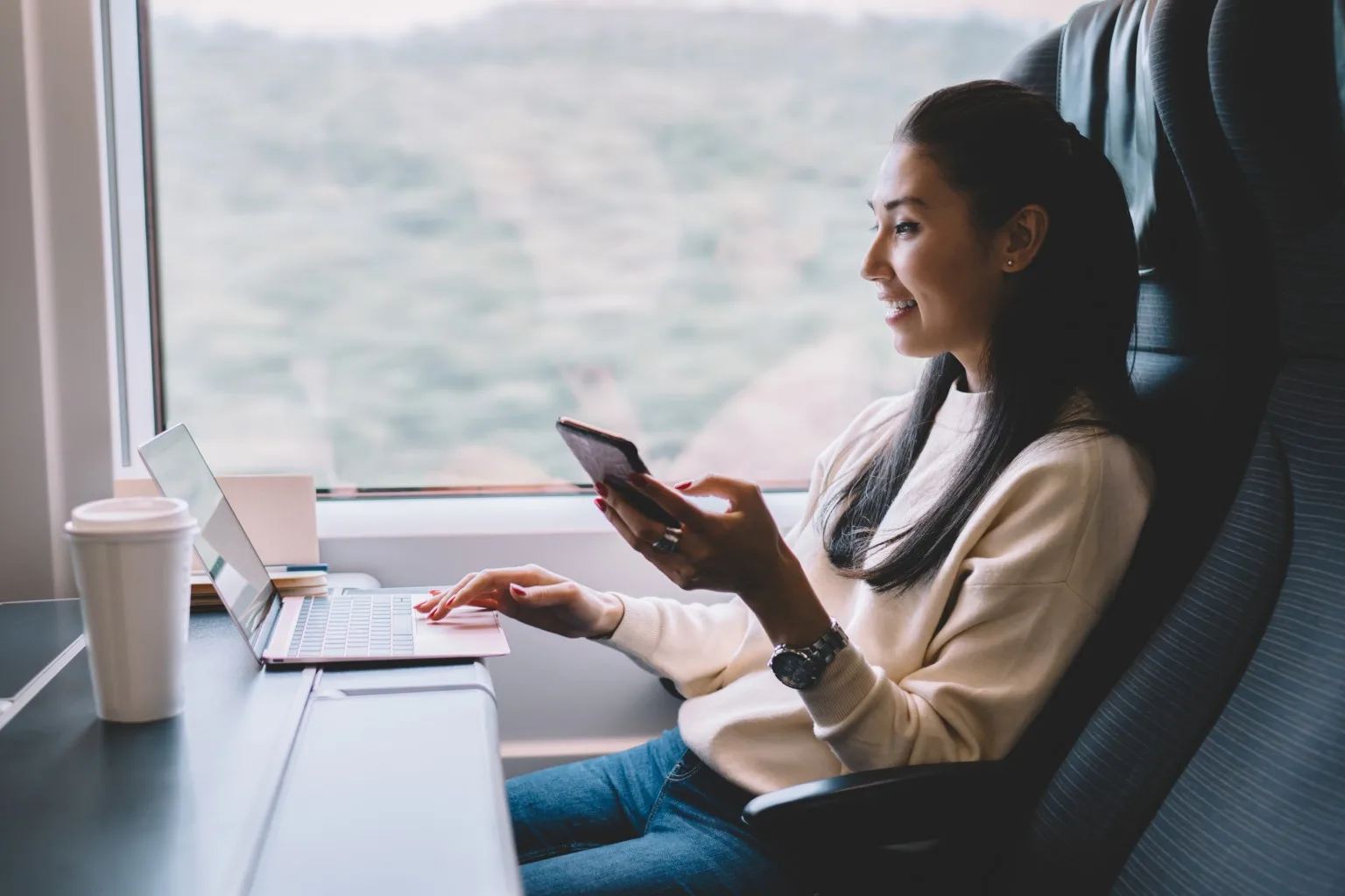 Woman sitting on train, with phone and laptop out.