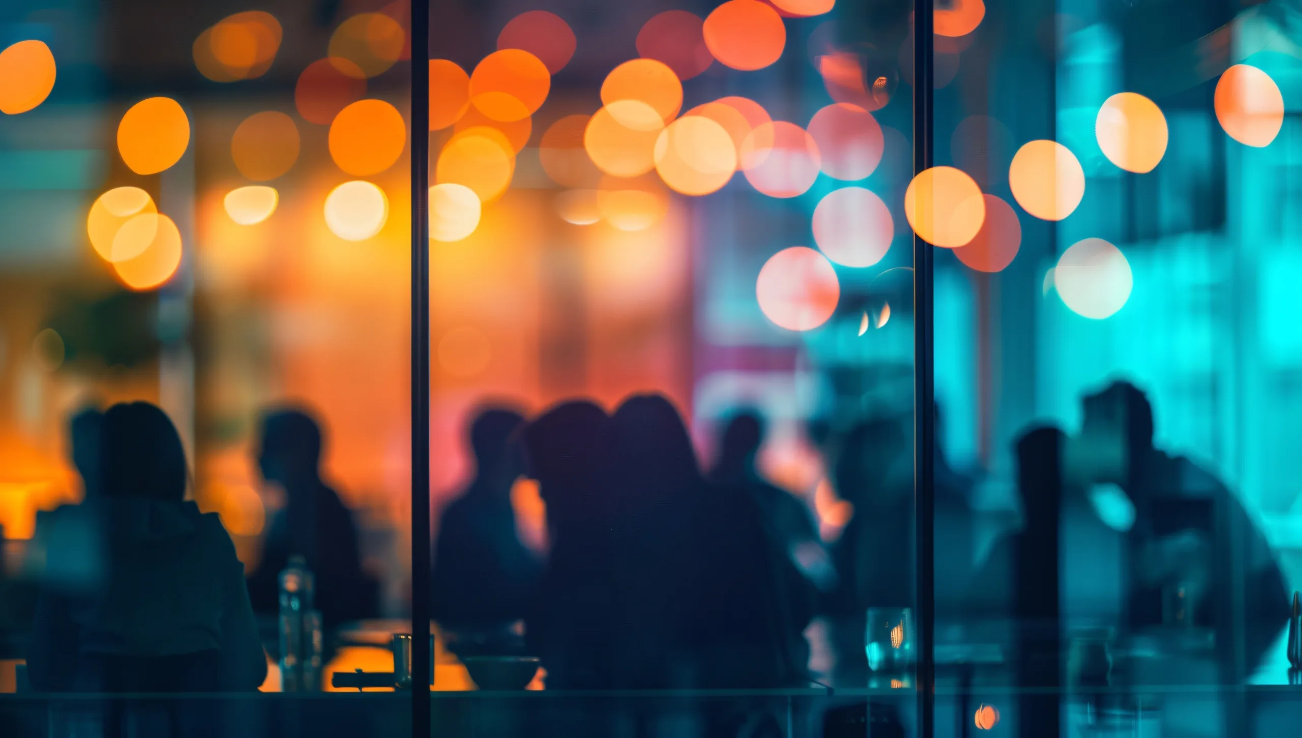 Blurred image through a window showing warm orange and cool blue bokeh lights with dark silhouettes of people in a restaurant or bar.