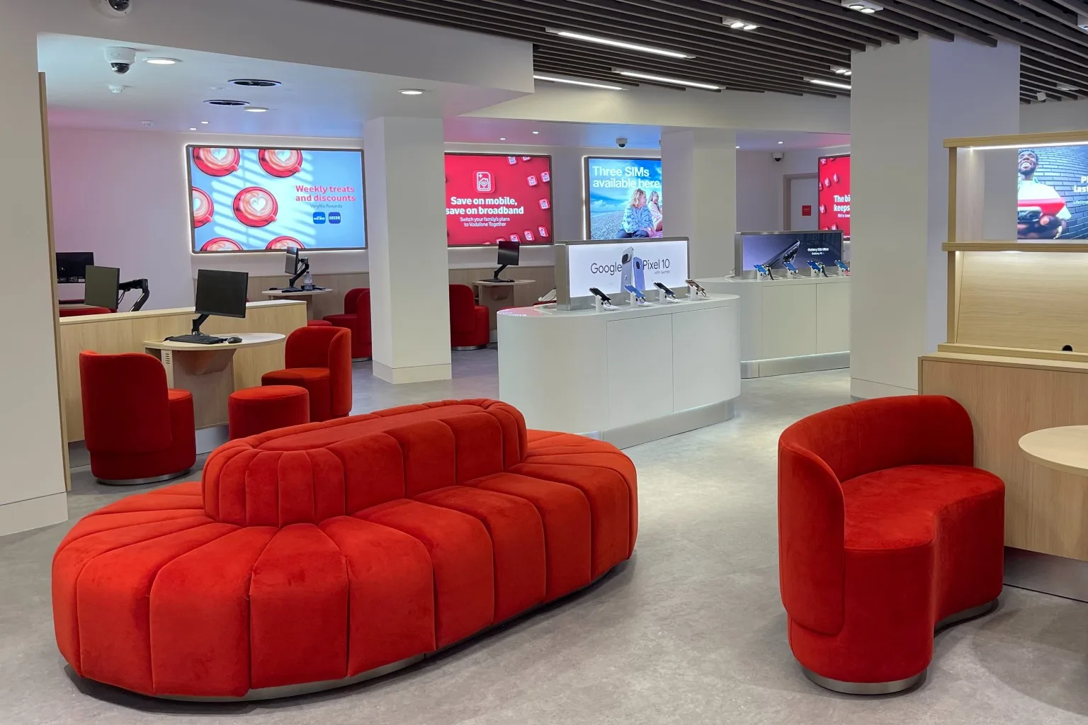 Interior of a modern retail store with red velvet seating, white display counters showcasing phones, and digital advertising screens.